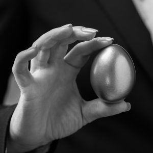 Close up of a female’s hand holding a gold egg, in black and white