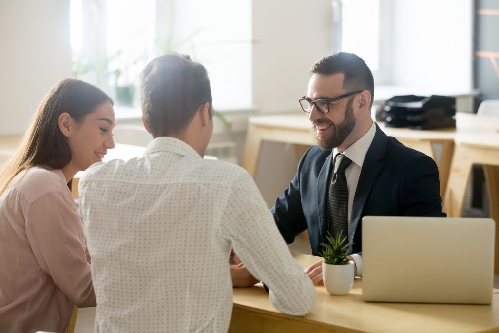 Smiling businessman sitting at desk with laptop and female and male client discussing insurance