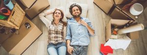 A couple laying on the floor holding hands with moving boxes all around them, post lockdown trends ruling the property market