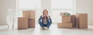 Happy lady sitting in an empty living room with moving boxes around her, mortgage markets recovery