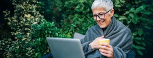 A mature lady sitting on a bench wrapped in a blanket looking at her pension age
