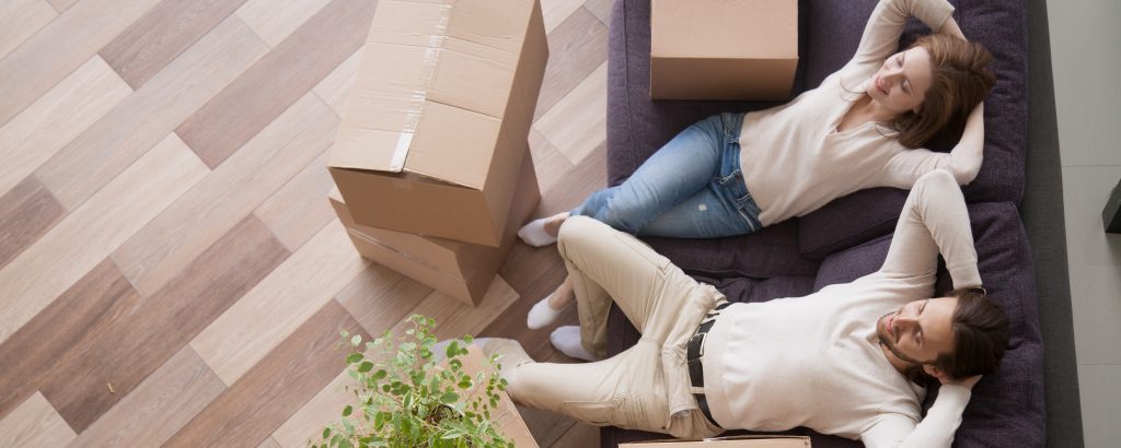 Young couple sitting on a sofa relaxing, with house moving boxes next to them and on the floor