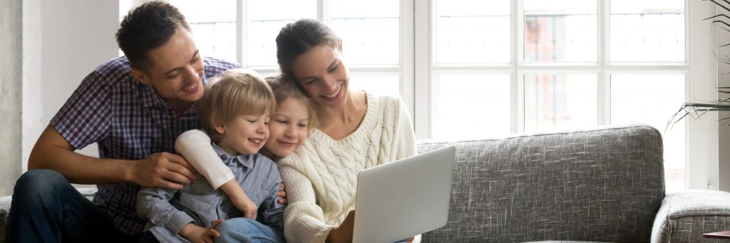 A family of Mum, Dad, brother and sister sat on a sofa looking at a laptop