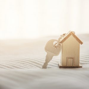 Symbol house with wood key on bed and sunlight, buy to let concept