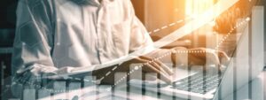 Business man on his laptop on a desk with paper graphs spread out and virtual arrow pointing up for growth