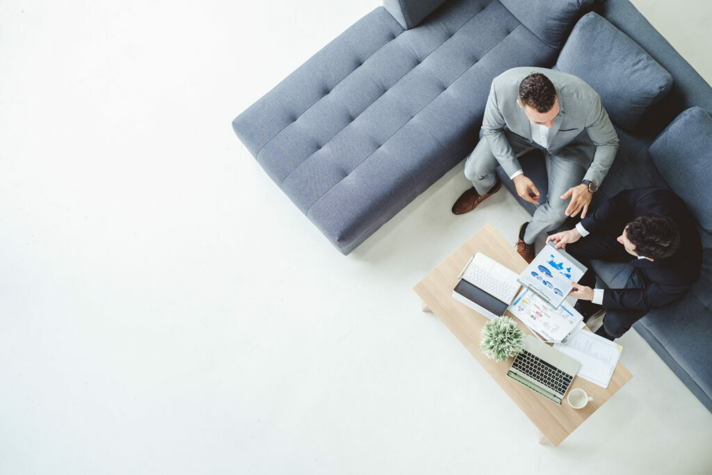 Two businessmen sitting round a coffee table with laptops, looking at graphs, planning to continue investing