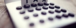 Wooden letters TAX sitting on calculator, people risking double tax hit on their pensions