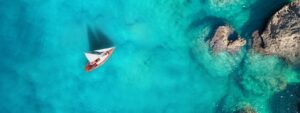 Aerial view of sail boat on clear, blue seas near coral reefs, endangered due to climate change