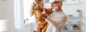 Smiling grandfather holding granddaughter in living room, older homeowners unlock cash for property