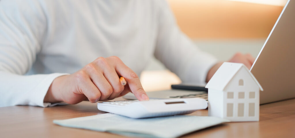 Lady at desk using a calculator with a model house in foreground and laptop behind, working out decrease in stamp duty