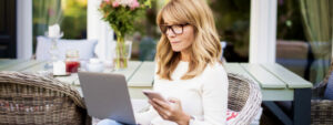 Lady sitting in garden chair, looking at laptop, phone in hand, checking finances, emotional wellbeing