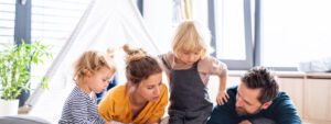 Front view of young family with two small children indoors in bedroom reading a book.