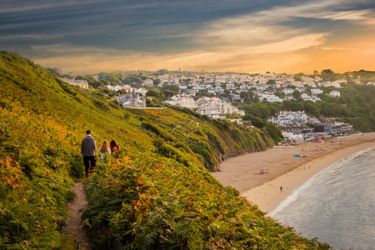 View of people walking in hilly seaside towards resort village in the bay at sunset
