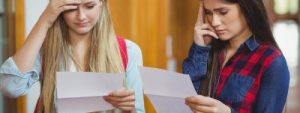 Two young girls at school reading their GCSE results letters looking concerned