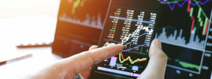 Businessman hand holding phone and looking at finance market graph of stock market trading on phone and laptop, investor sentiment remaining positive