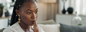 Stress, anxiety and woman biting nails in home with fear, worry and mental health risk. Face of african girl in living room with crisis of trauma, nervous habit and overthinking with doubt of mistake