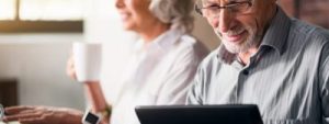 Older couple sitting the kitchen reading the news on a laptop and tablet